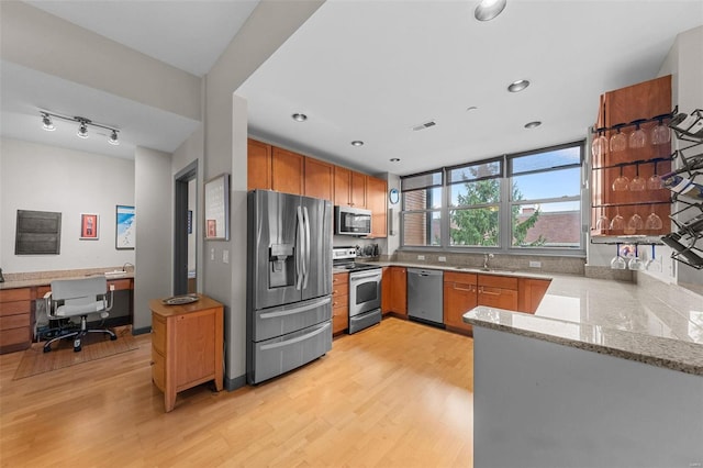 kitchen with brown cabinetry, light wood-style flooring, appliances with stainless steel finishes, light stone counters, and a sink