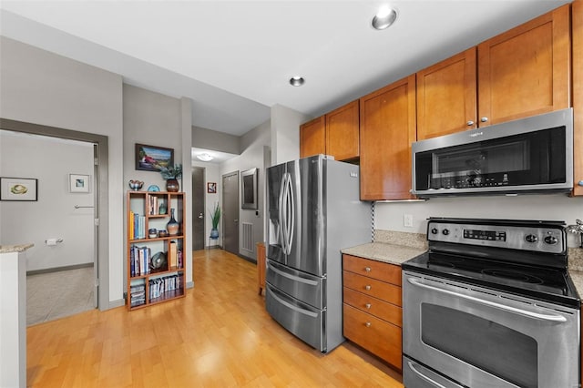 kitchen featuring brown cabinetry, light stone counters, stainless steel appliances, and light wood finished floors