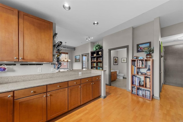 kitchen with brown cabinetry, light wood-style flooring, light stone counters, and a peninsula