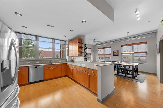 kitchen featuring light wood-style flooring, appliances with stainless steel finishes, brown cabinetry, a sink, and a peninsula