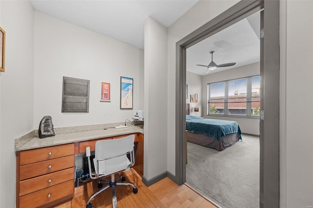 interior space featuring light colored carpet, light wood-style floors, built in study area, ceiling fan, and baseboards