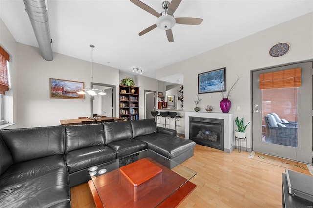 living room featuring ceiling fan, light wood-type flooring, and a glass covered fireplace