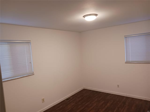 empty room featuring baseboards, visible vents, and dark wood-style flooring