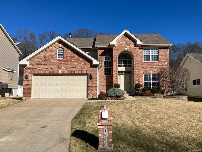 traditional-style house featuring a front yard, an attached garage, brick siding, and driveway