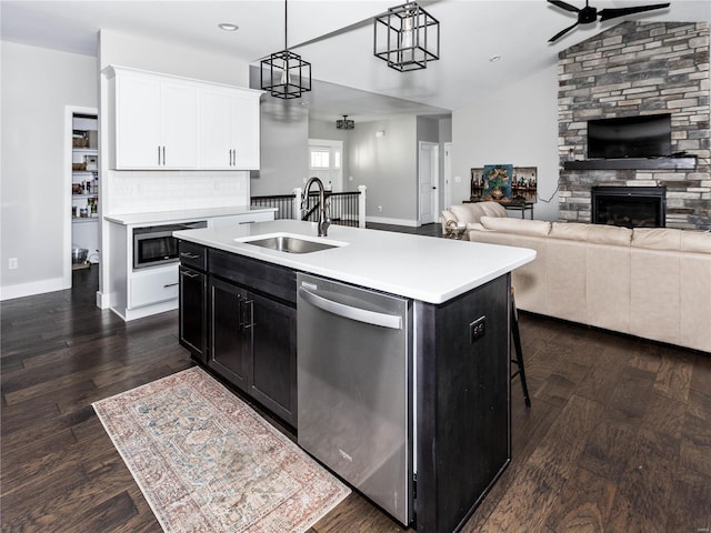 kitchen with dishwasher, light countertops, a stone fireplace, dark cabinetry, and a sink