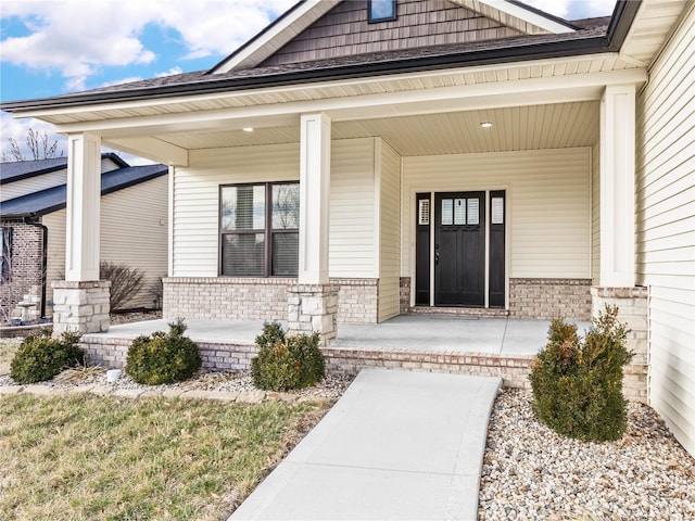 view of exterior entry with brick siding and a porch