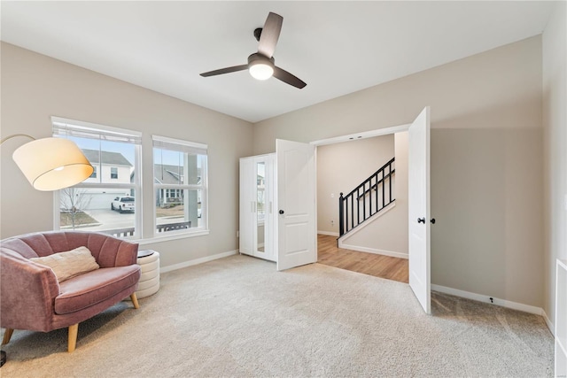 sitting room with carpet floors, ceiling fan, baseboards, and stairs