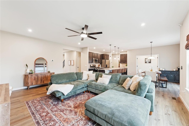 living room with light wood-type flooring, baseboards, a ceiling fan, and recessed lighting