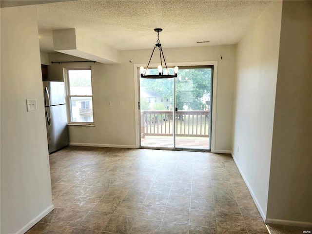 spare room featuring a chandelier, a wealth of natural light, a textured ceiling, and baseboards