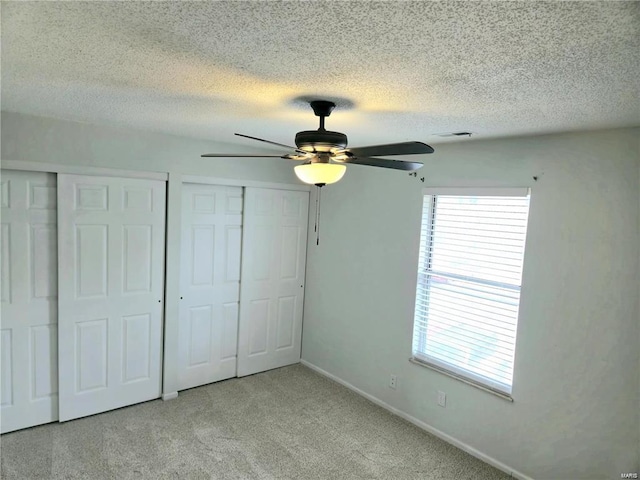 unfurnished bedroom with carpet floors, multiple closets, ceiling fan, a textured ceiling, and baseboards