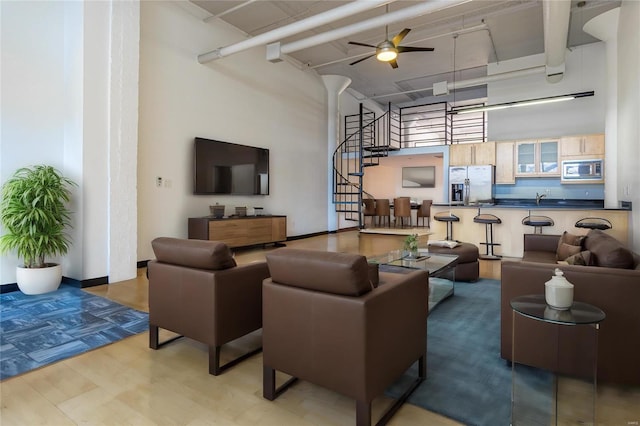 living area featuring stairs, ceiling fan, a towering ceiling, and baseboards