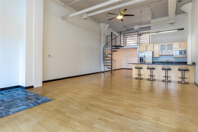 unfurnished living room with a high ceiling, a ceiling fan, wood finished floors, baseboards, and stairs