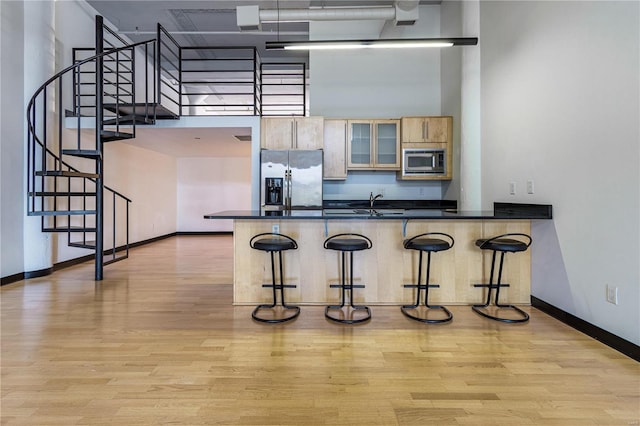 kitchen with stainless steel appliances, a peninsula, a towering ceiling, a kitchen breakfast bar, and light wood-style floors