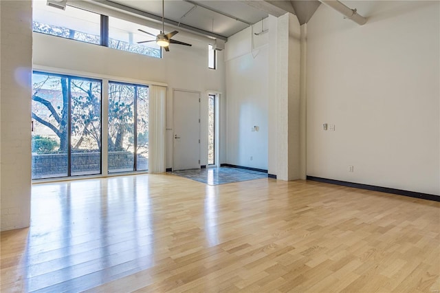 empty room featuring ceiling fan, wood finished floors, a towering ceiling, and baseboards