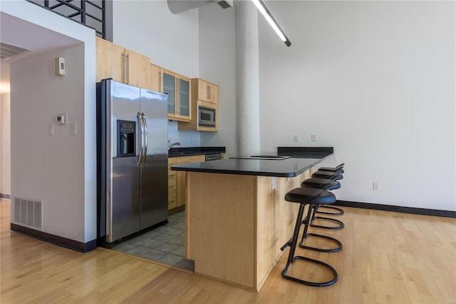 kitchen featuring light brown cabinets, stainless steel appliances, visible vents, a kitchen breakfast bar, and dark countertops