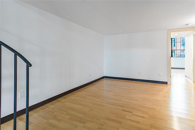 spare room with baseboards, stairway, and light wood finished floors