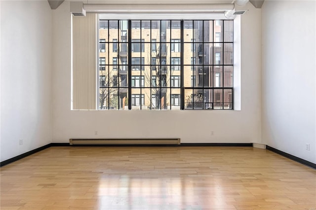 empty room with a baseboard radiator, wood finished floors, and baseboards