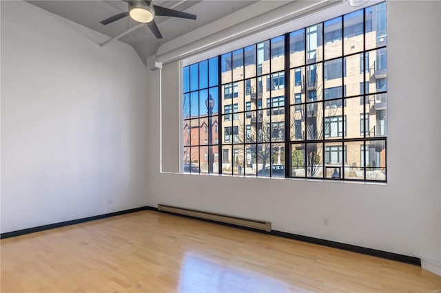 spare room with a ceiling fan, a baseboard radiator, baseboards, and wood finished floors