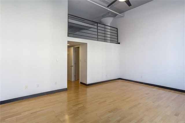 unfurnished room featuring ceiling fan, a high ceiling, baseboards, and wood finished floors