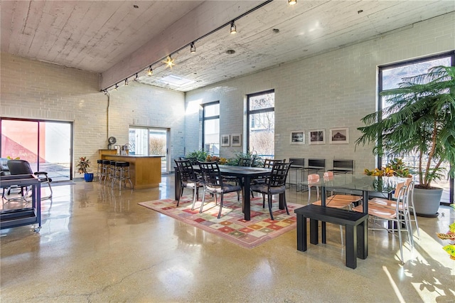 dining room featuring track lighting, brick wall, a high ceiling, and speckled floor