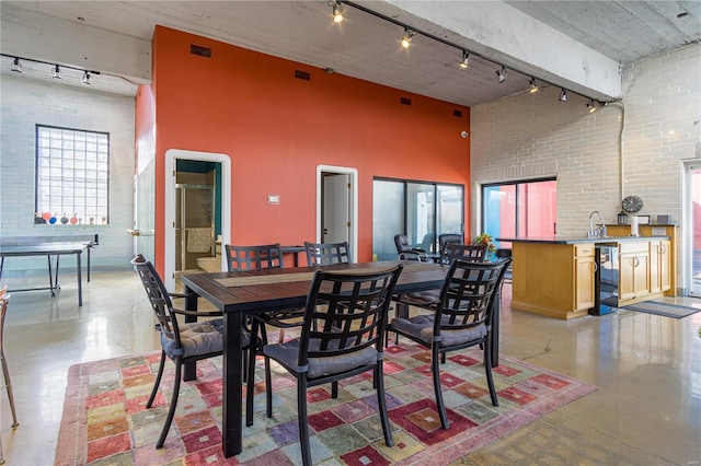 dining room featuring visible vents, rail lighting, a towering ceiling, brick wall, and beverage cooler