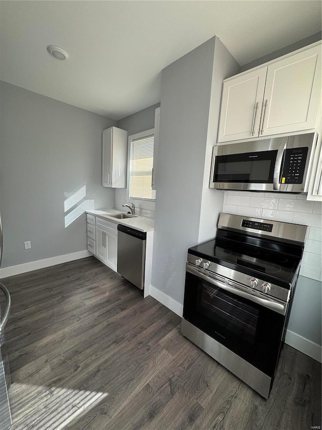 kitchen featuring dark wood-style floors, stainless steel appliances, white cabinetry, a sink, and baseboards