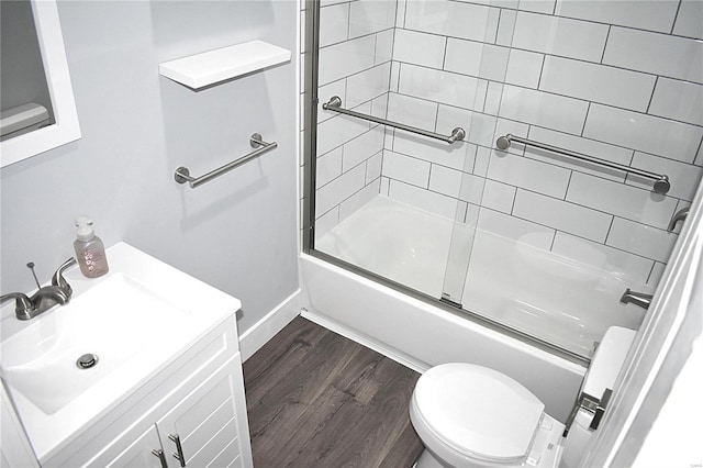 bathroom with baseboards, bath / shower combo with glass door, toilet, wood finished floors, and vanity