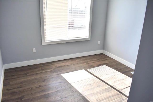 spare room with baseboards and dark wood-type flooring