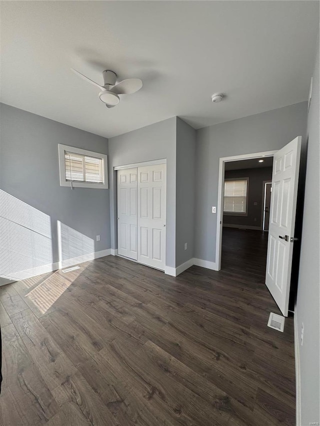 unfurnished bedroom with dark wood-style flooring, a closet, visible vents, ceiling fan, and baseboards