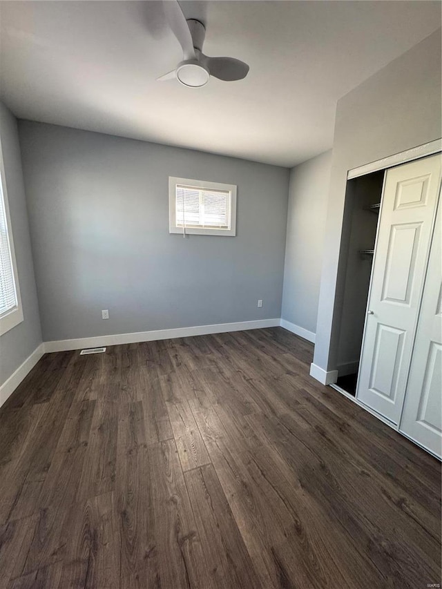 unfurnished bedroom with dark wood-type flooring, a closet, a ceiling fan, and baseboards