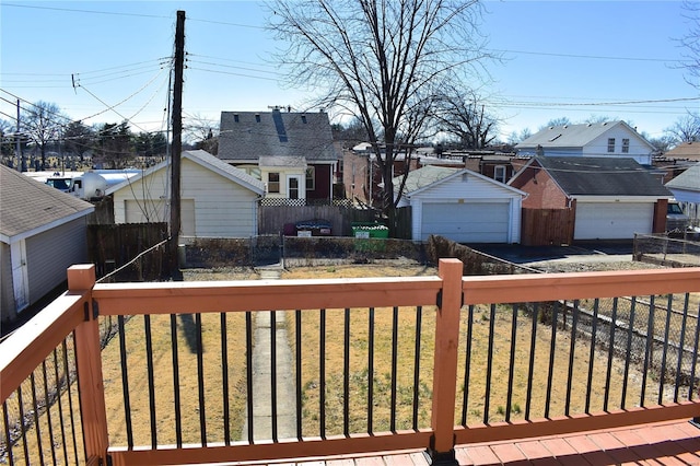 wooden terrace featuring a residential view, a detached garage, fence, and an outbuilding