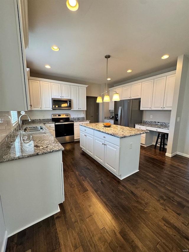 kitchen featuring dark wood-style floors, a kitchen island, appliances with stainless steel finishes, white cabinetry, and a sink