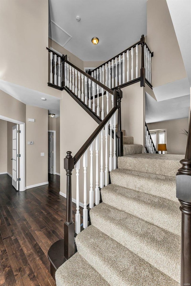 stairway with a high ceiling, wood finished floors, and baseboards