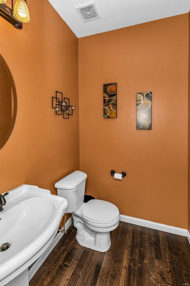 bathroom with baseboards, visible vents, toilet, wood finished floors, and a sink