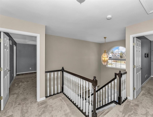 hallway with baseboards, carpet flooring, an upstairs landing, and an inviting chandelier