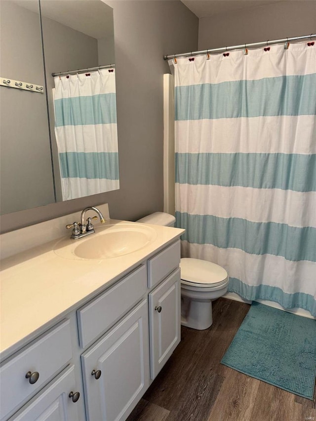 bathroom featuring toilet, a shower with shower curtain, wood finished floors, and vanity