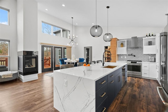 kitchen with wall chimney range hood, dark wood-style floors, white cabinets, stainless steel appliances, and a sink