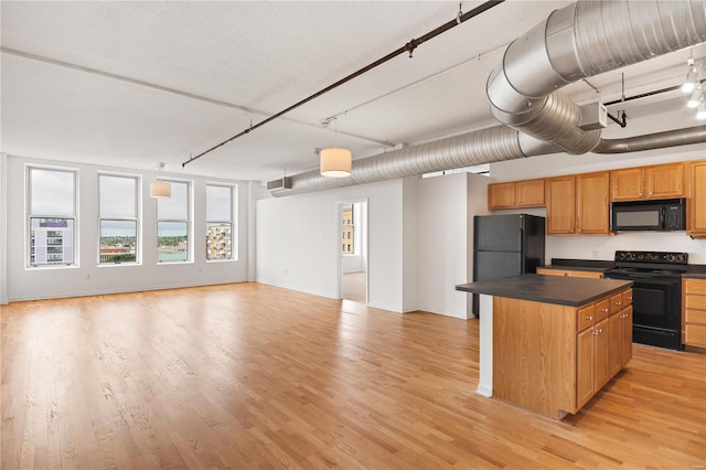 kitchen featuring dark countertops, light wood-style flooring, open floor plan, a center island, and black appliances