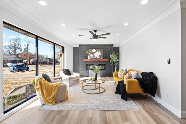 living room with recessed lighting, wood finished floors, baseboards, ornamental molding, and a glass covered fireplace