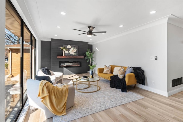 living area with visible vents, ornamental molding, a glass covered fireplace, wood finished floors, and baseboards