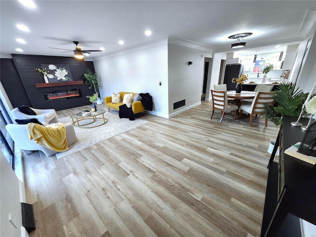 living area featuring baseboards, light wood-type flooring, a glass covered fireplace, and crown molding