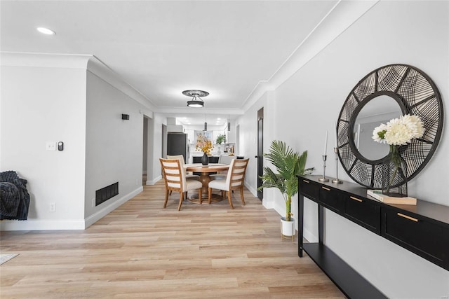 dining room with ornamental molding, light wood-type flooring, visible vents, and baseboards