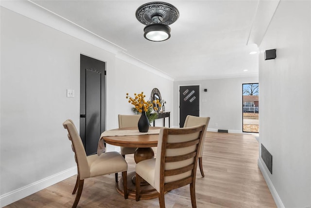 dining room with light wood-style floors, visible vents, baseboards, and crown molding