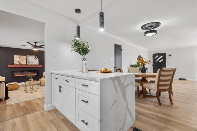 kitchen featuring decorative light fixtures, light wood finished floors, a glass covered fireplace, white cabinetry, and light stone countertops