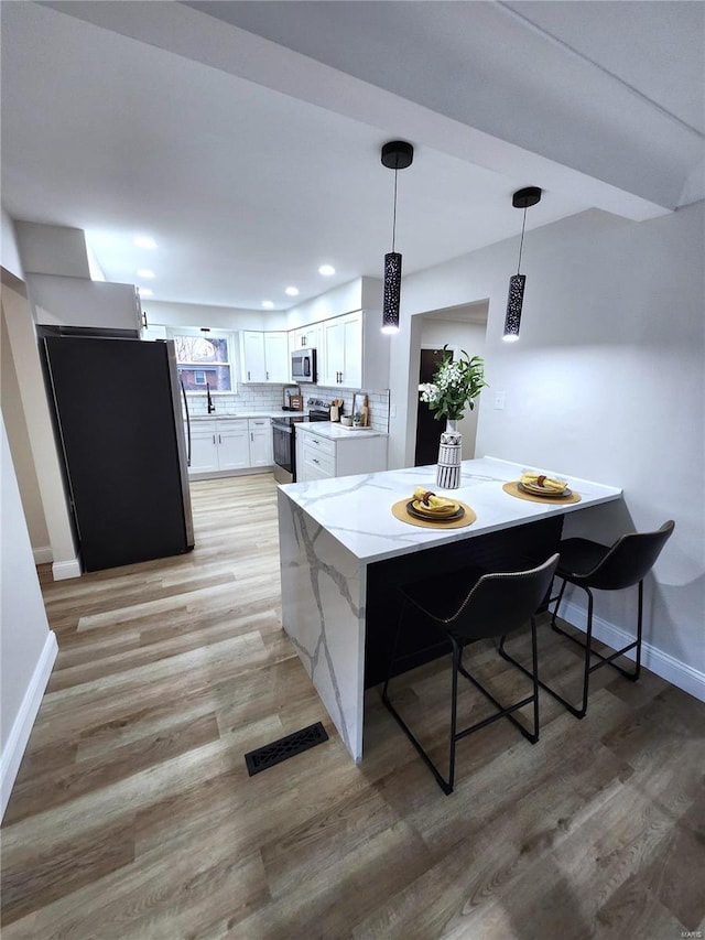 kitchen featuring light wood-style flooring, visible vents, stainless steel appliances, and backsplash