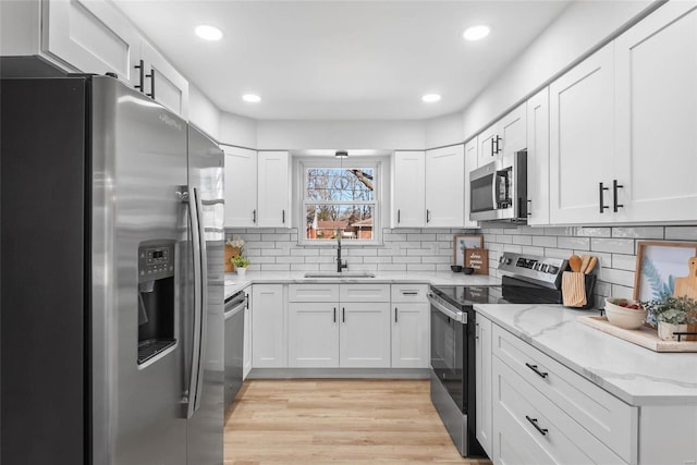 kitchen with a sink, white cabinetry, light wood-style floors, appliances with stainless steel finishes, and light stone countertops