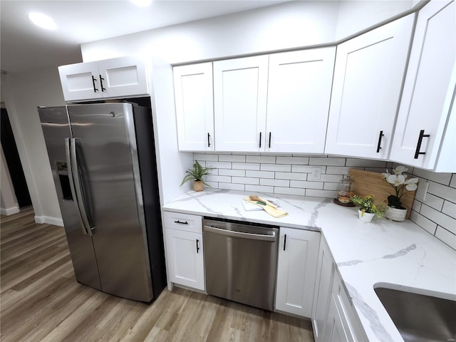 kitchen featuring light wood-style flooring, appliances with stainless steel finishes, white cabinets, and backsplash