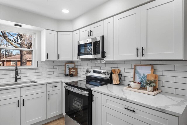 kitchen with light stone counters, a sink, white cabinetry, appliances with stainless steel finishes, and tasteful backsplash