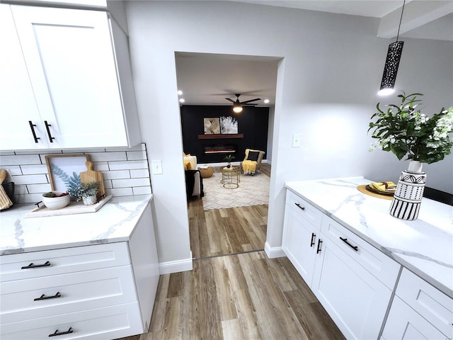 kitchen with a warm lit fireplace, tasteful backsplash, light wood-type flooring, and white cabinets