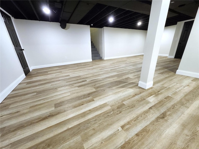 finished basement with stairway, light wood-style flooring, and baseboards